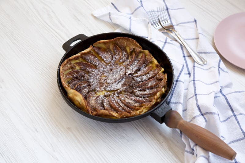 Homemade Apple Dutch Pannekoek Pancake in a cast-iron pan on a white wooden background, side view