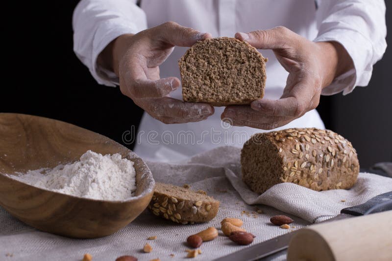 A male chef`s hand present and cutting whole grain bread with gold knife and pouring flour. A male chef`s hand present and cutting whole grain bread with gold knife and pouring flour.