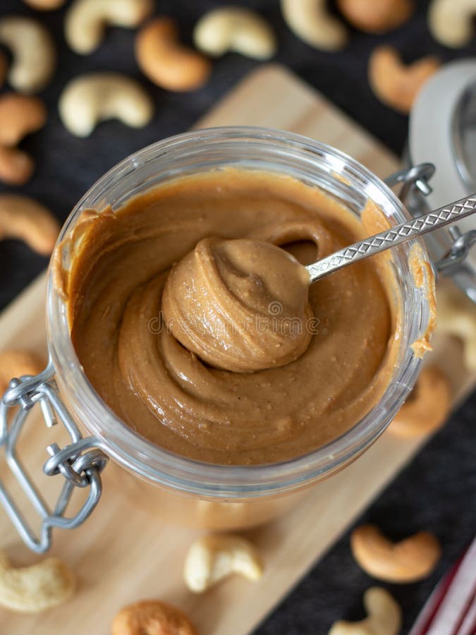 Homemade cashew butter in a jar with spoon on a dark background, vertical shot, top view. Homemade cashew butter in a jar with spoon on a dark background