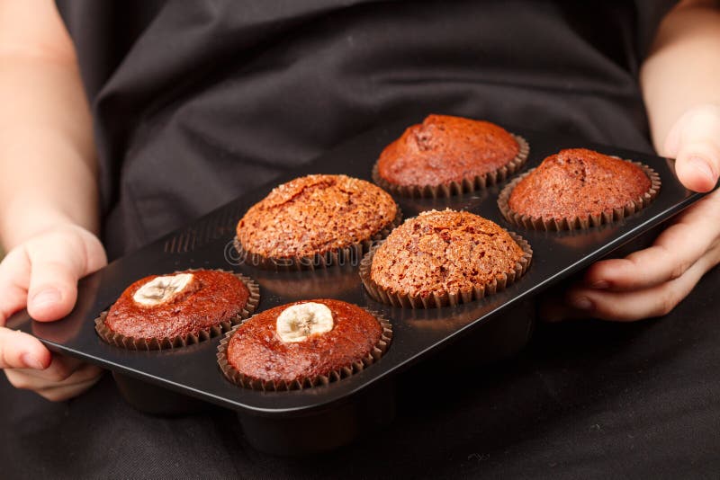Homemade chocolate, banana and caramel muffins in a baking dish in the children`s hands royalty free stock photos Homemade chocolate, banana and caramel muffins in a baking dish in the children`s hands royalty free stock photos