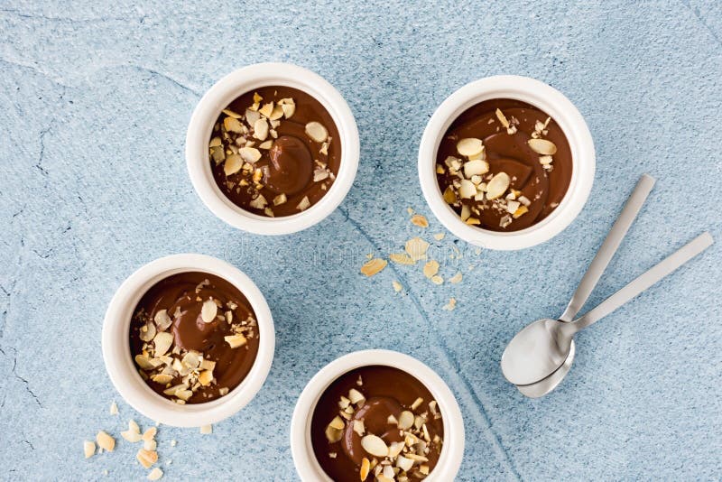 Homemade chocolate pudding in three white ceramic ramekins with roasted almond slivers and teaspoons on light blue concrete royalty free stock photo Homemade chocolate pudding in three white ceramic ramekins with roasted almond slivers and teaspoons on light blue concrete royalty free stock photo