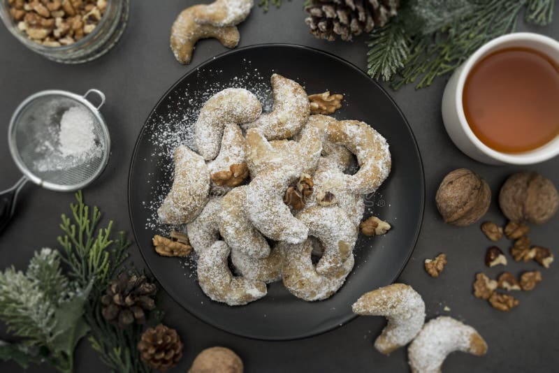 Homemade Christmas cookies with nuts, cup of tea and winter decorations over dark background. Top view