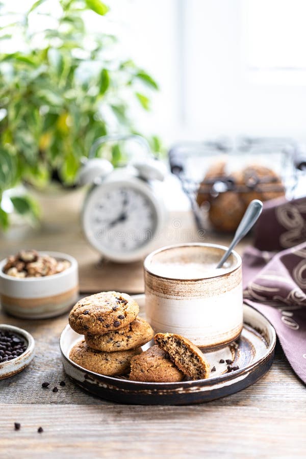 Homemade cookies with nuts and coffee in a ceramic cup on a wooden table. Time to drink some coffee. Alarm clock in the background. Breakfast.