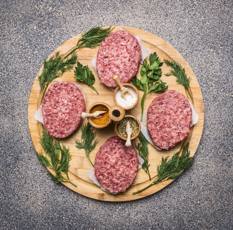 Homemade cutlet of beef for burgers, lined circle on a round wooden chopping board parsley and dill and spices royalty free stock photography Homemade cutlet of beef for burgers, lined circle on a round wooden chopping board parsley and dill and spices royalty free stock photography