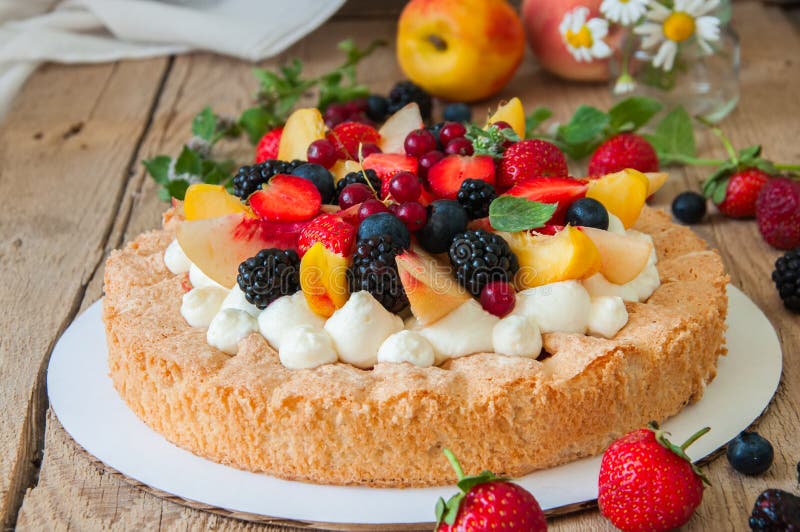 Homemade dacquoise cake with wipped cream cheese garnished with summer berries and peaches, close up.