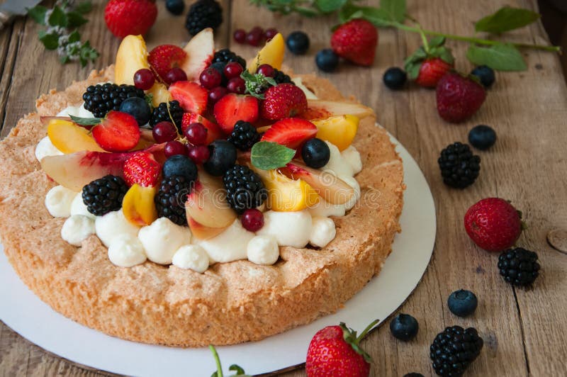 Homemade dacquoise cake with wipped cream cheese garnished with summer berries and peaches, close up.