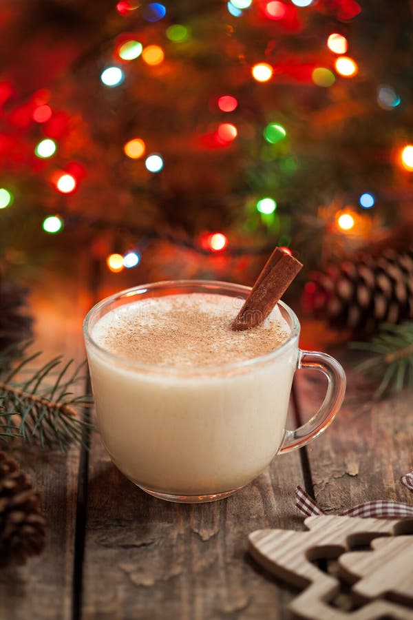 Homemade eggnog, egg milk vanilla rum, alcohol liqueur in glass with cinnamon stick on vintage wooden table. Colorful bokeh background, shallow depth of field. Rustic style.