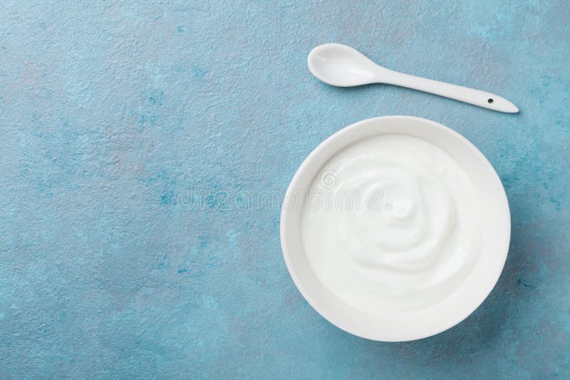 Homemade greek yogurt in bowl on blue stone table top view.