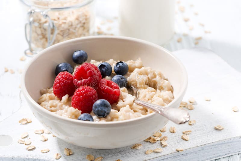 Homemade oatmeal with berries on white wooden board, closeup