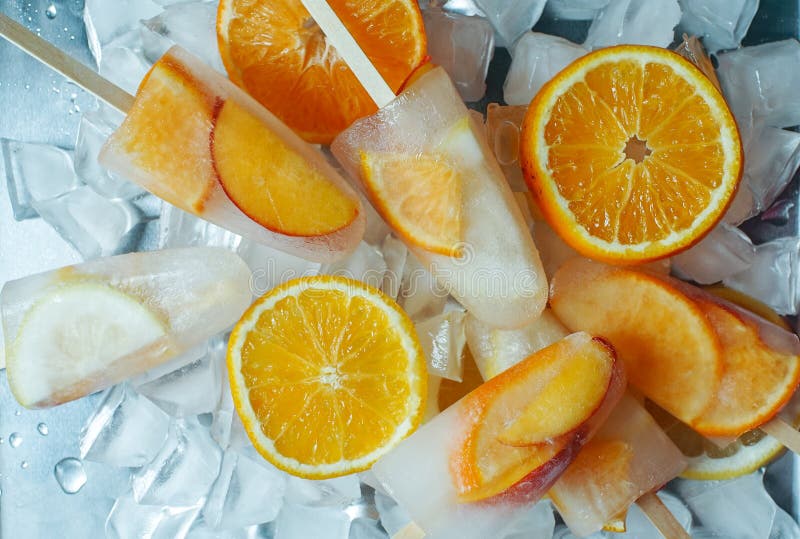 Homemade orange and peach popsicles with ice and citrus slices on light background