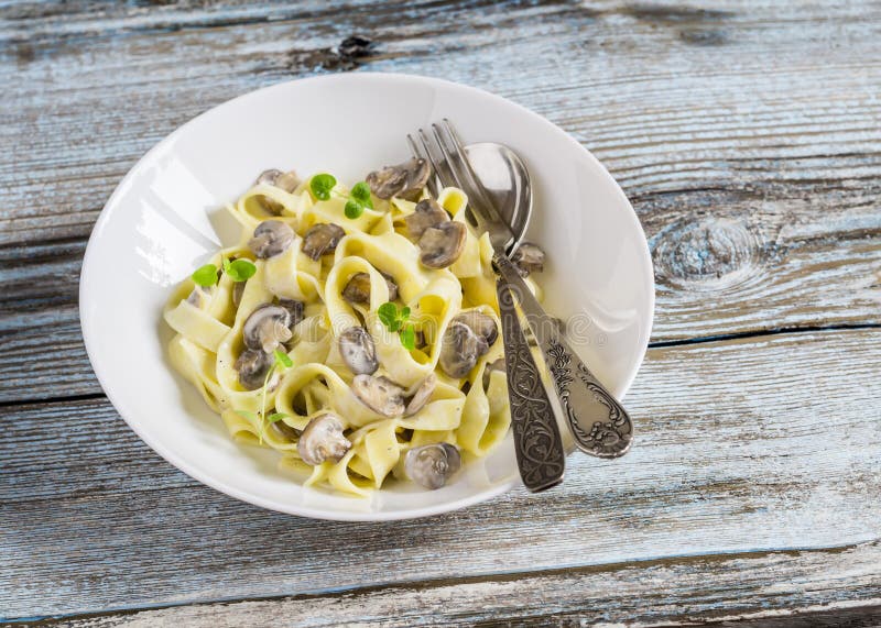 Homemade pasta with creamy mushroom sauce on a light wooden background.