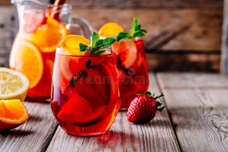 Homemade red wine sangria with orange, apple, strawberry and ice in glass and pitcher on wooden background