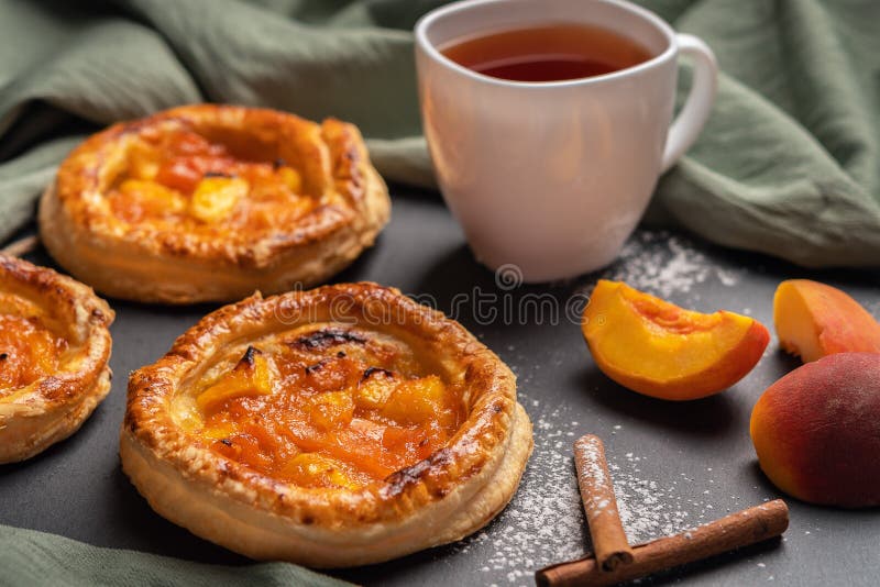 Homemade round puffs with peaches on a dark background with a linen napkin. Next to white cup with black tea, peach slices, royalty free stock image Homemade round puffs with peaches on a dark background with a linen napkin. Next to white cup with black tea, peach slices, royalty free stock image