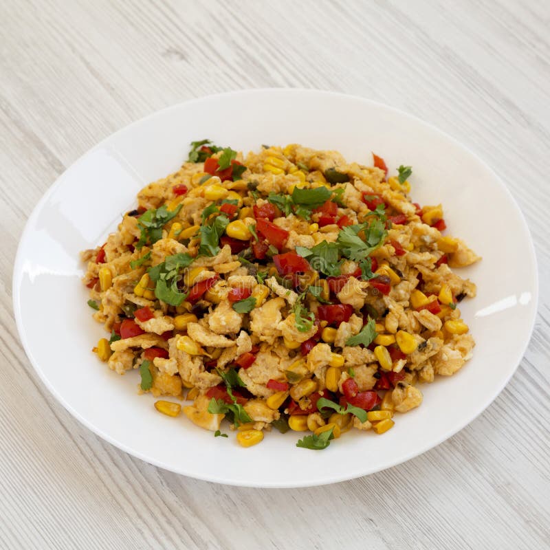 Homemade southwestern egg scramble on a white plate on a white wooden background, side view. Close-up