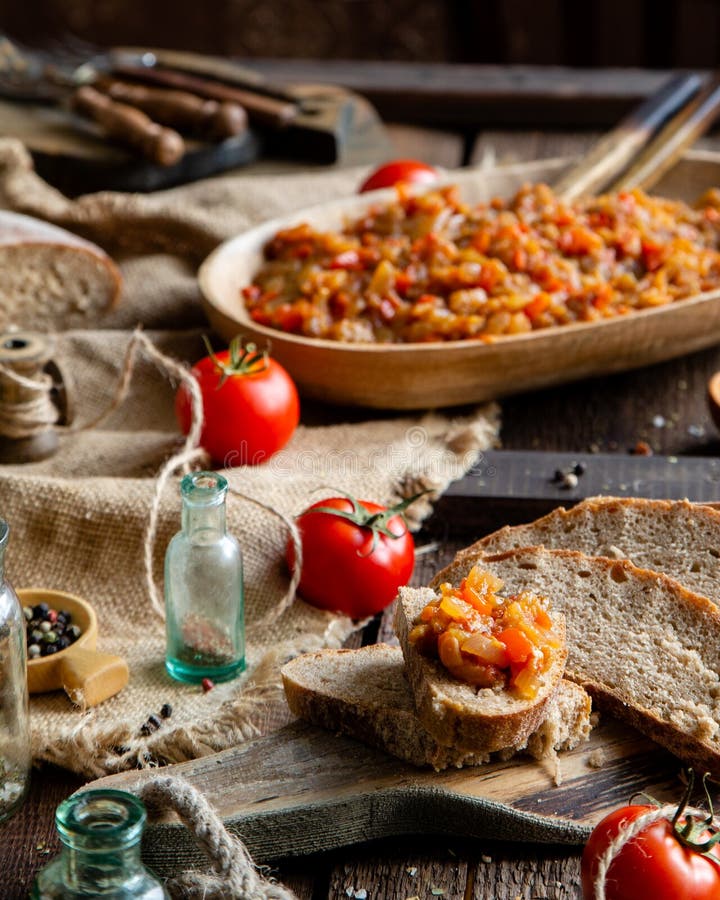 Homemade tasty orange vegetable caviar, ratatouille or ragout on slices of bread and in oval wooden dish on rustic brown table. With old bottles, bowl with stock images Homemade tasty orange vegetable caviar, ratatouille or ragout on slices of bread and in oval wooden dish on rustic brown table. With old bottles, bowl with stock images