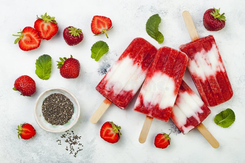 Homemade vegan strawberry coconut milk popsicles with chia seeds on rustic white background.