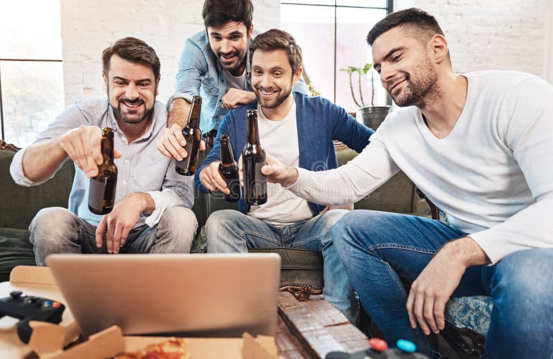 Homens alegres felizes que bebem a cerveja com seus amigos em linha imagens de stock Homens alegres felizes que bebem a cerveja com seus amigos em linha imagens de stock