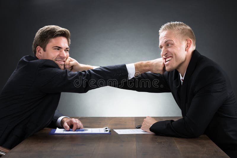 Homens de negócios novos que lutam na mesa de madeira imagem de stock Homens de negócios novos que lutam na mesa de madeira imagem de stock