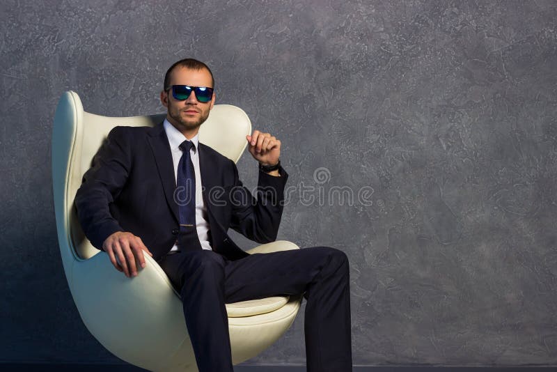 Homens de negócios 'sexy' brutais no terno com laço e óculos de sol que sentam-se na cadeira imagem de stock Homens de negócios 'sexy' brutais no terno com laço e óculos de sol que sentam-se na cadeira imagem de stock