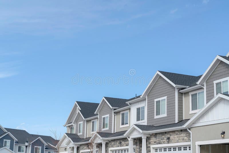 Homes with gable roofs and gray exterior walls against blue sky in the suburbs