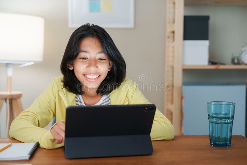 Homeschooling, Asian girl doing homework and online learning with tutor on the tablet digital while sitting  at a desk at night