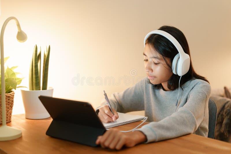 Homeschooling, asiatisk flicka som gör läxor och onlinekurser med handledare på surfplattan digitalt med hörlurar hemma natten arkivfoton