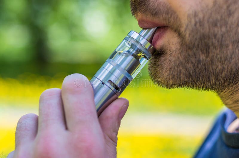 Homme adulte fumant une e-cigarette de vape en parc images libres de droits Homme adulte fumant une e-cigarette de vape en parc images libres de droits