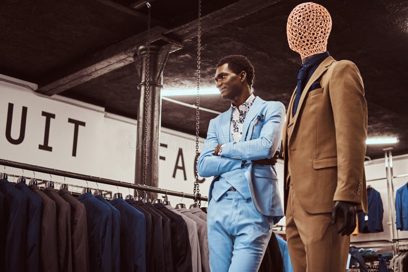 Homme afro-américain d'une manière élégante habillé posant avec les bras croisés près du mannequin dans un magasin classique de v photographie stock libre de droits Homme afro-américain d'une manière élégante habillé posant avec les bras croisés près du mannequin dans un magasin classique de v photographie stock libre de droits