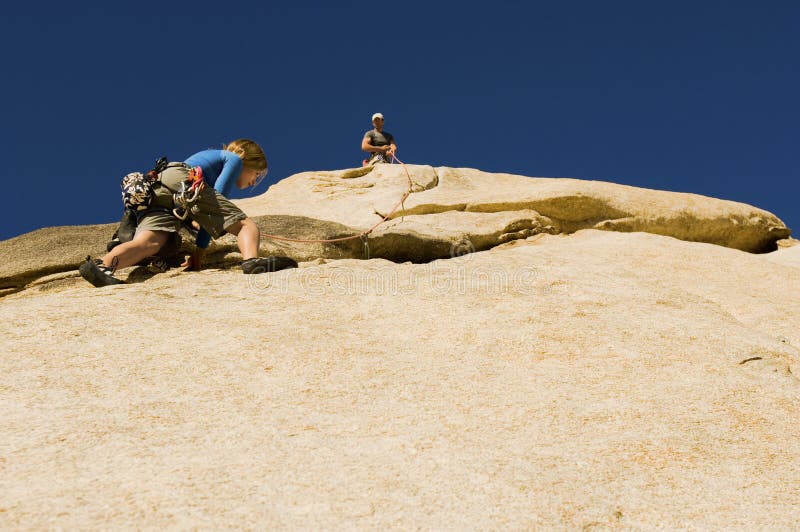 Low angle view of men assisting friend climbing rock against clear blue sky. Low angle view of men assisting friend climbing rock against clear blue sky