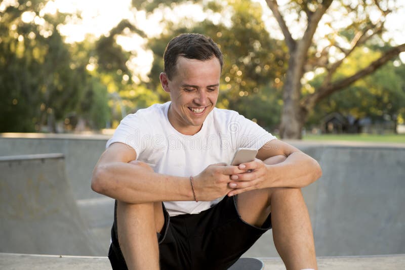 Homme américain 30s s'asseyant sur le panneau de patin après stage de formation d'embarquement de sport utilisant le téléphone po