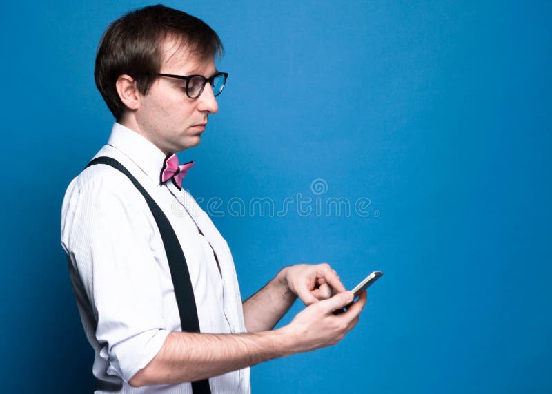 Homme aux cheveux sombres en chemise rose avec manches roulées, cravate, suspense noire et lunettes utilisant un smarphone photos stock Homme aux cheveux sombres en chemise rose avec manches roulées, cravate, suspense noire et lunettes utilisant un smarphone photos stock