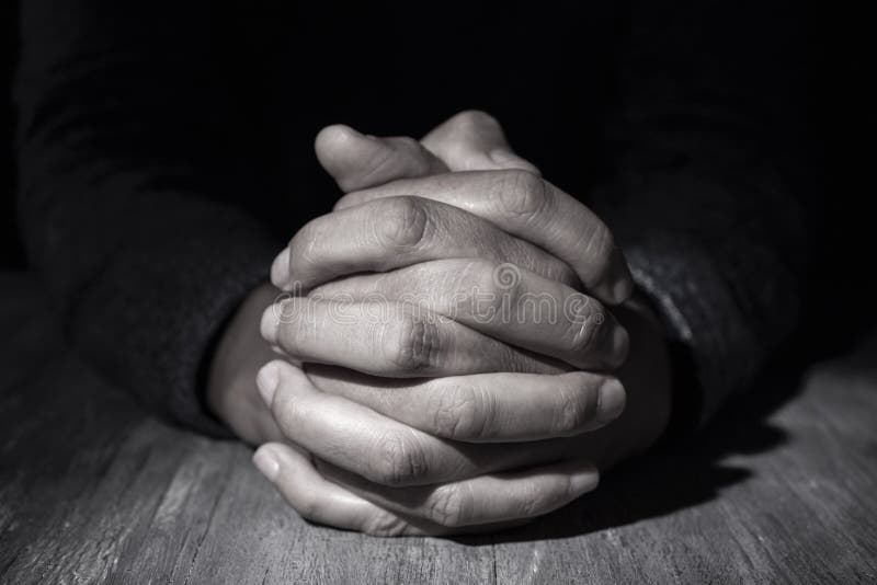 Closeup of the hands of a young caucasian man with his hands clasped on a wooden table. Closeup of the hands of a young caucasian man with his hands clasped on a wooden table