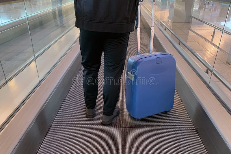 Homme avec une valise sur des roues, photographiées par derrière, à l'aéroport sur un passage couvert mobile photos stock Homme avec une valise sur des roues, photographiées par derrière, à l'aéroport sur un passage couvert mobile photos stock