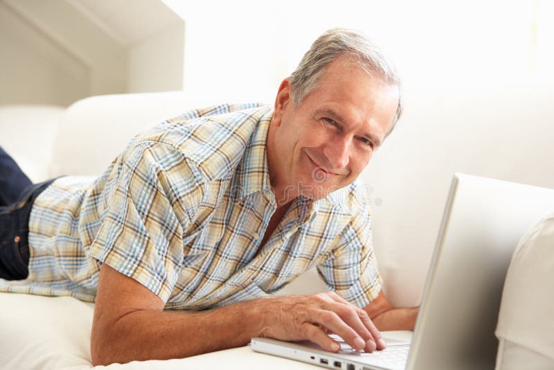 Homme aîné utilisant se reposer de détente d'ordinateur portatif sur le sofa photos stock Homme aîné utilisant se reposer de détente d'ordinateur portatif sur le sofa photos stock
