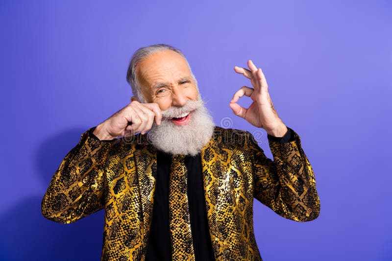Homme barbu excentrique en blouson d'or gestant avec confiance contre un fond violet vibrant images libres de droits