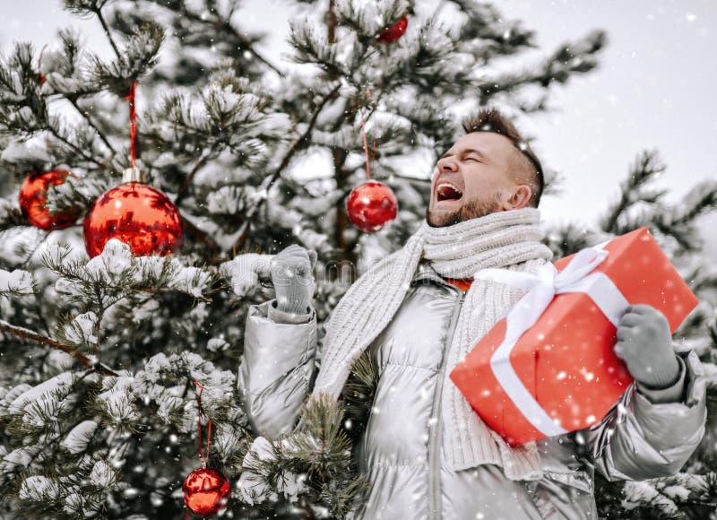 Homme barbu heureux dans hurlait vers le bas des détenteurs de manteau à l'arbre de Noël décoré avec le rouge giftbox extérieur