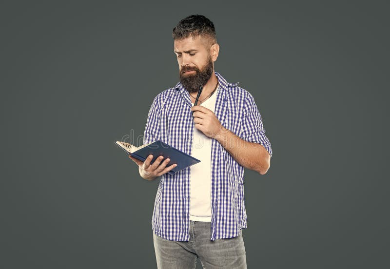 Homme barbu sérieux faisant des notes dans le livre sur fond gris photographie stock libre de droits