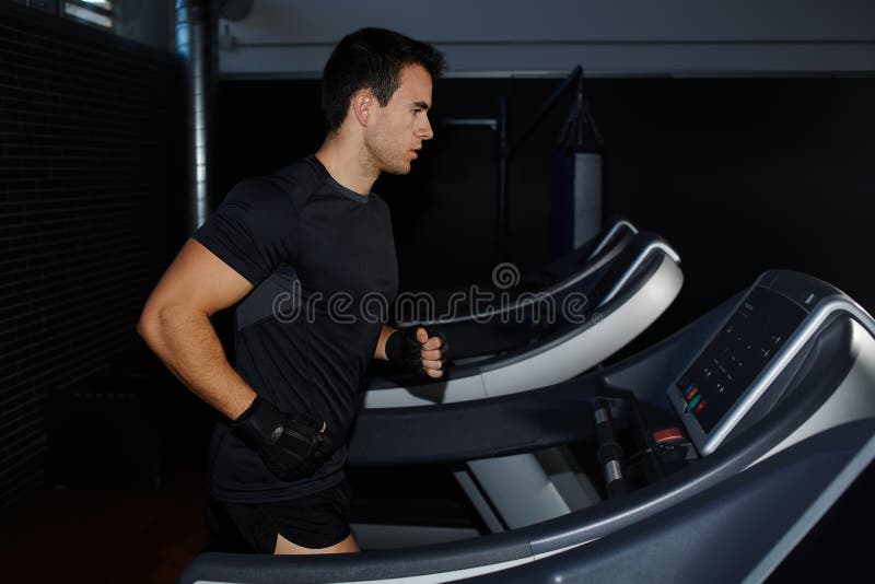 Homme bel de brune faisant la séance d'entraînement dans le gymnase fonctionnant sur le tapis roulant images stock Homme bel de brune faisant la séance d'entraînement dans le gymnase fonctionnant sur le tapis roulant images stock