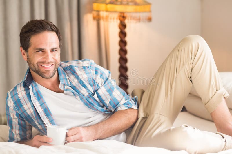Homme bel détendant sur son lit avec la boisson chaude photographie stock libre de droits Homme bel détendant sur son lit avec la boisson chaude photographie stock libre de droits