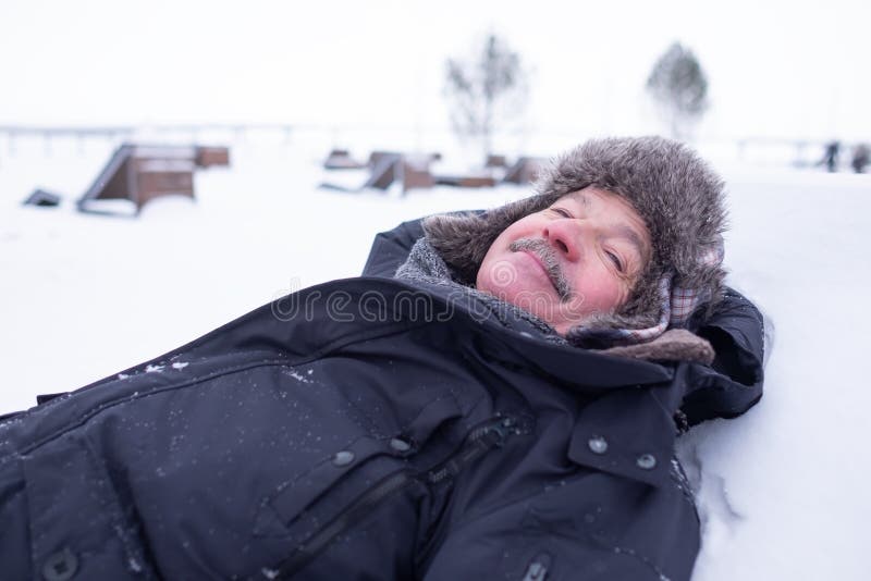 Homme bel supérieur dans les vêtements chauds et le chapeau se trouvant sur la neige et rêver images stock Homme bel supérieur dans les vêtements chauds et le chapeau se trouvant sur la neige et rêver images stock