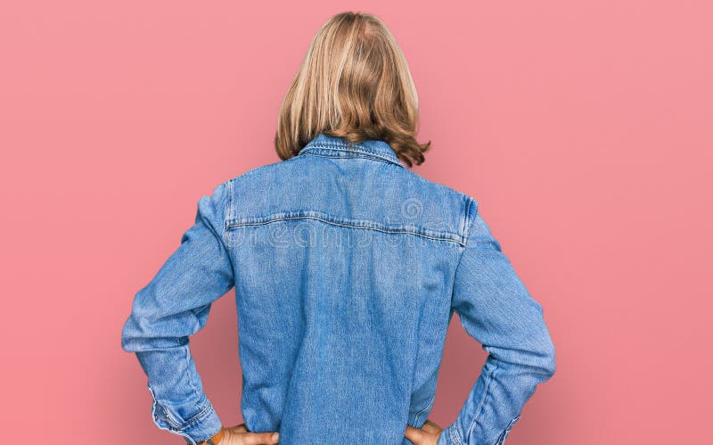 Homme caucasien avec blond cheveux longs portant casual veste en denim debout à l'arrière regardant loin avec les bras sur le corp photographie stock libre de droits
