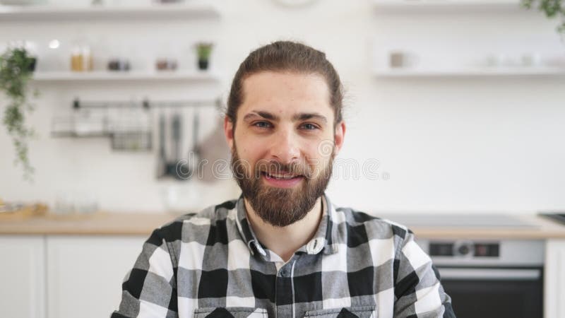 Homme caucasien en chemise à damier assis au bureau sur fond de cuisine.