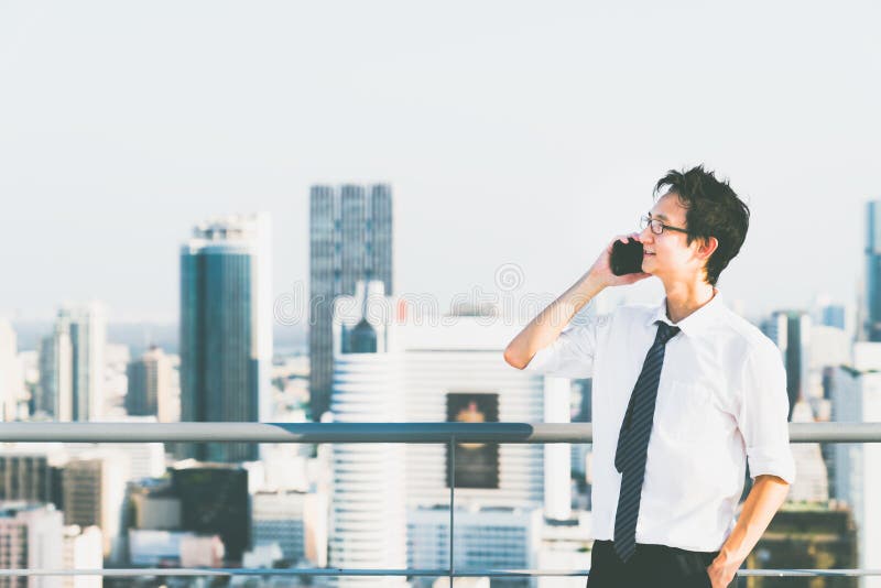 Homme d'affaires asiatique utilisant le faire appel de téléphone portable au dessus de toit de bâtiment, l'espace de copie sur le photographie stock libre de droits Homme d'affaires asiatique utilisant le faire appel de téléphone portable au dessus de toit de bâtiment, l'espace de copie sur le photographie stock libre de droits
