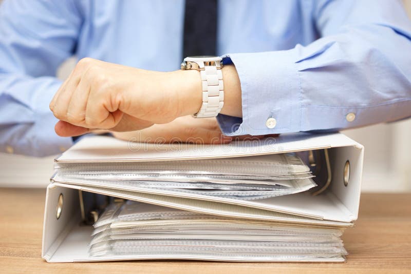 Homme d'affaires avec la pile de documentation sur le bureau regardant sur W image stock Homme d'affaires avec la pile de documentation sur le bureau regardant sur W image stock