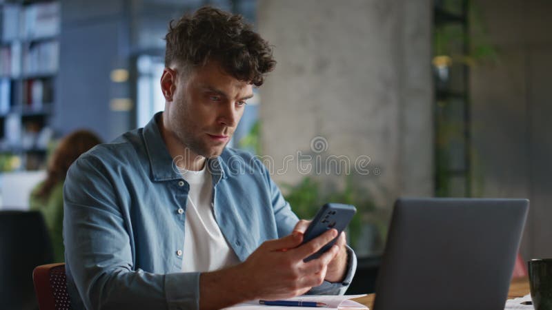 Homme d'affaires concentré recherche smartphone lecture messages à la table ordinateur portable closeuse banque de vidéos