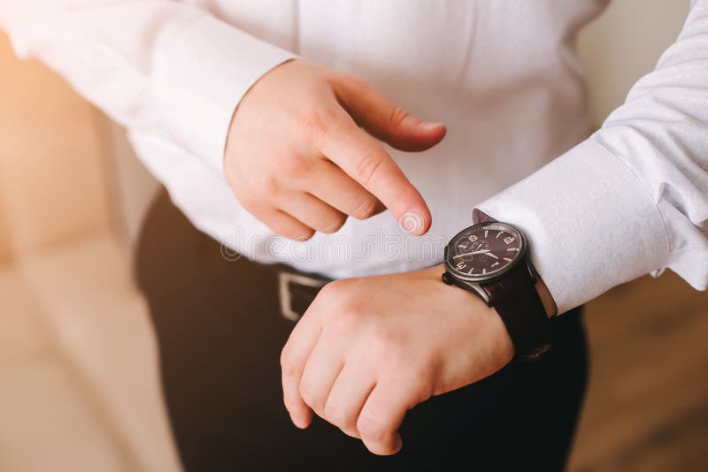 Homme d'affaires dans la chemise blanche regardant sa montre-bracelet suisse sur sa main et observant le temps photo libre de droits Homme d'affaires dans la chemise blanche regardant sa montre-bracelet suisse sur sa main et observant le temps photo libre de droits