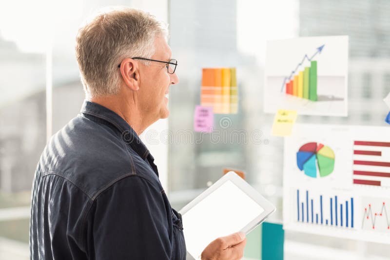 Homme d'affaires de sourire regardant des organigrammes sur le mur photographie stock Homme d'affaires de sourire regardant des organigrammes sur le mur photographie stock