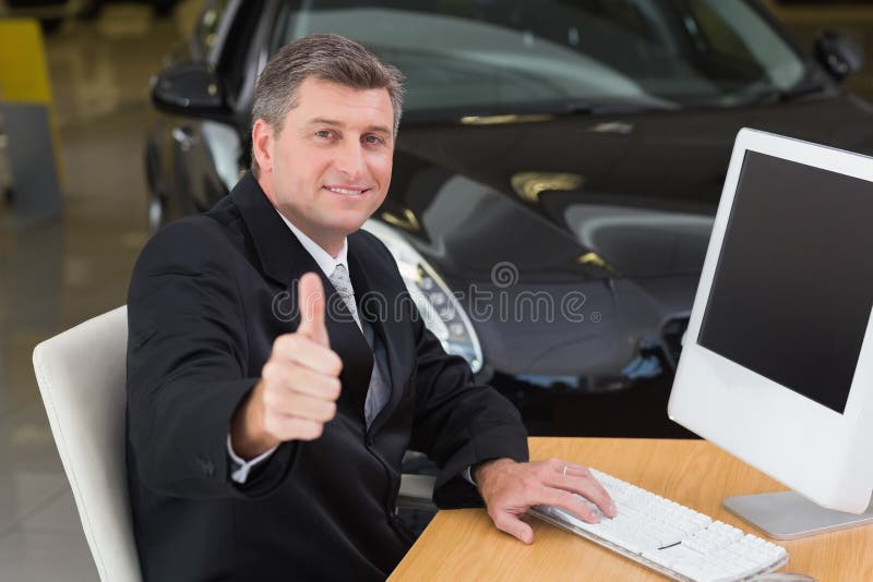 Homme d'affaires de sourire renonçant à des pouces à son bureau photo stock Homme d'affaires de sourire renonçant à des pouces à son bureau photo stock