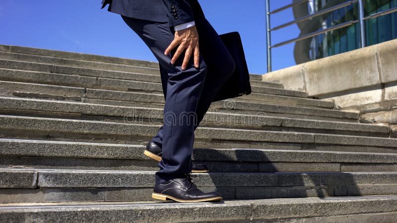 Homme d'affaires descendant des escaliers sentant la douleur forte de genou, inflammation commune images stock Homme d'affaires descendant des escaliers sentant la douleur forte de genou, inflammation commune images stock
