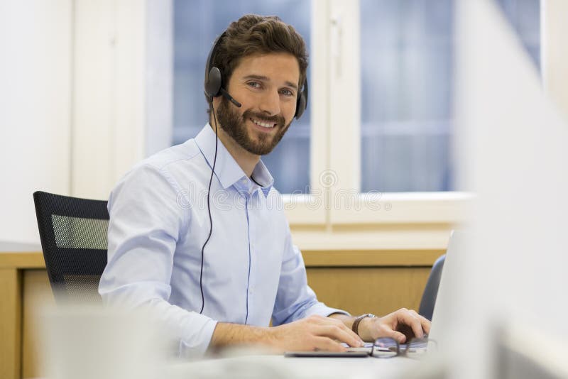 Homme d'affaires gai dans le bureau au téléphone, casque, Skype images stock Homme d'affaires gai dans le bureau au téléphone, casque, Skype images stock